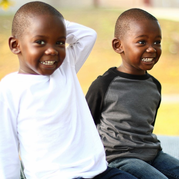 Two young twin brothers sit together and smile.