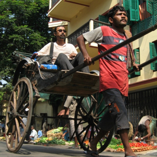 A rickshaw driver pulls a passenger down a city street.