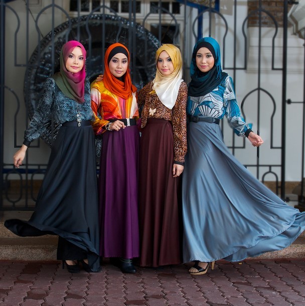 A group of Malaysian fashion models pose in colorful headscarves, long-sleeved blouses, and floor-length dresses.