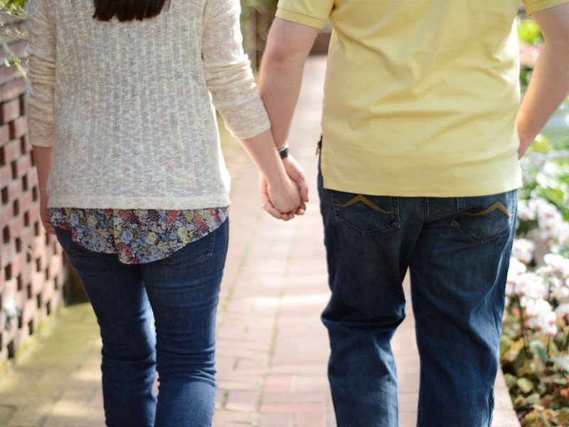 A couple holding hands as they walk down the sidewalk.