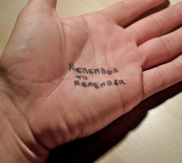 A note is written on a man's hand which says, "remember to remember".