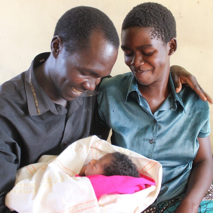 A young mother and father are all smiles as they hold their infant.