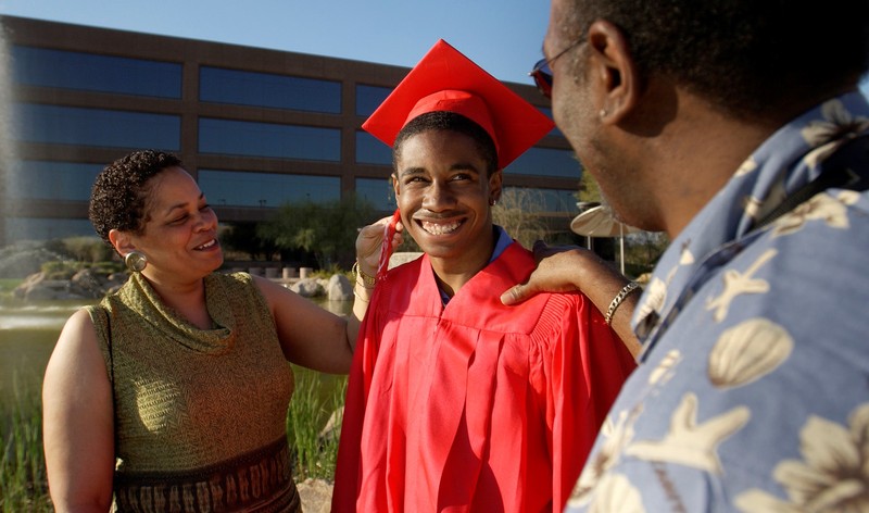 Smiling parents stand with their young adult son who is dressed in a graduation cap and gown.