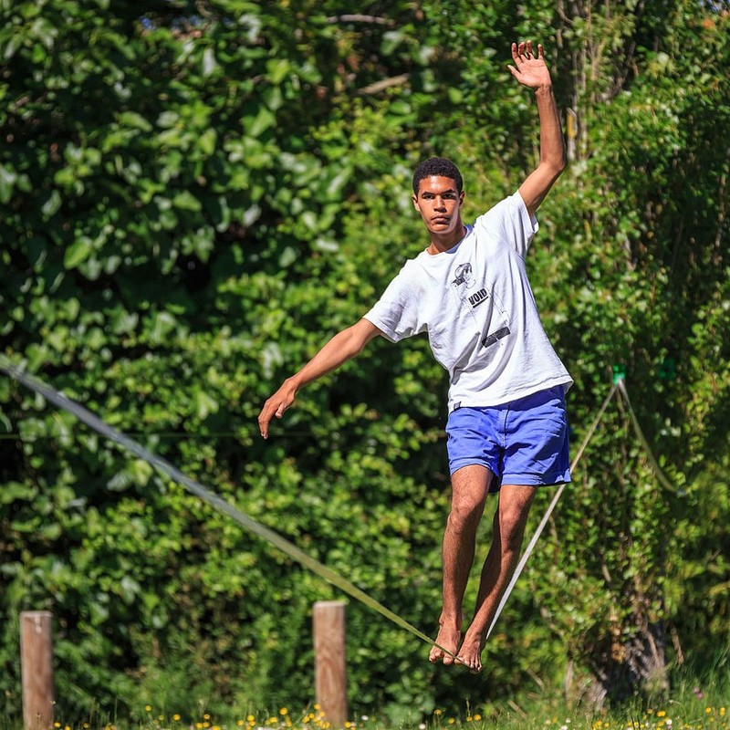 A man walks across a slackline with his arms extended for balance.
