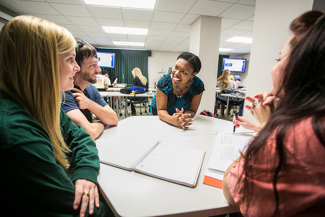 An instructor enjoys a discussion with a group of students during a class.