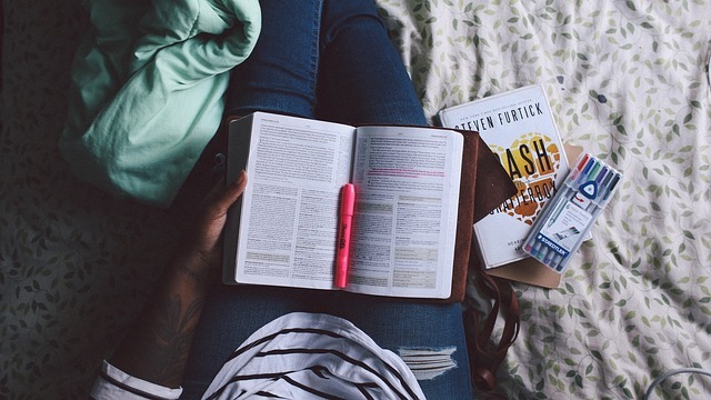 A student sits with an open book in her lap and a set of highlight markers close by.