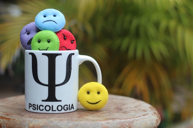 A cup with round plushies depicting various human emotions such as joy or sadness. The cup has a Greek letter Psi on it and a word Psicologia written on it.